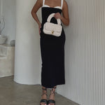 Video of a model holding a white knitted crossbody handbag with gold clasps against a white wall.