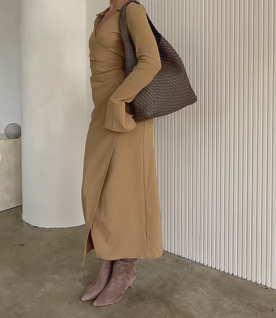 Video of a model wearing a large woven vegan leather shoulder bag against a white wall.