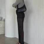 Video fo a model wearing a asymmetrical vegan leather shoulder bag against a white wall. 