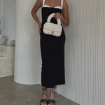Video of a model holding a ivory knitted crossbody handbag against a white wall. 