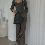 Video of a model wearing a small woven wide strap tote bag against a white wall. 