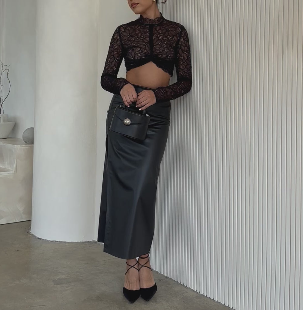 Video of a model wearing a small recycled vegan leather top handle bag against a white wall.