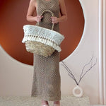 Video of a model wearing a large straw woven tote bag with seashell details and drawstring closure.