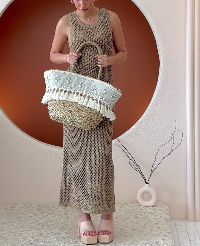 Video of a model wearing a large straw woven tote bag with seashell details and drawstring closure.