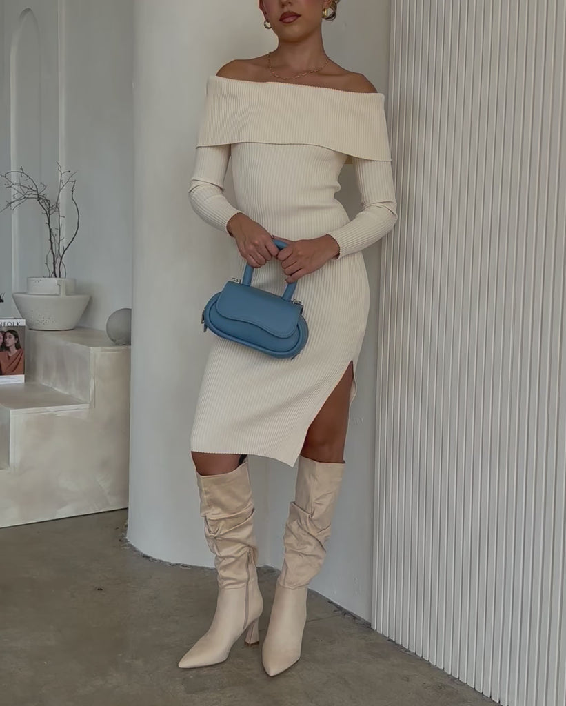Video of a model wearing a sky oval shaped crossbody handbag against a white wall. 