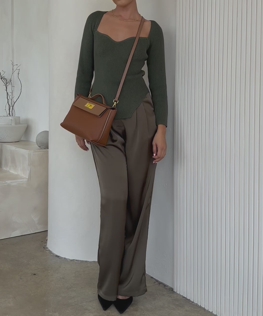 Video of a model wearing a saddle medium vegan leather crossbody bag against a white wall. 
