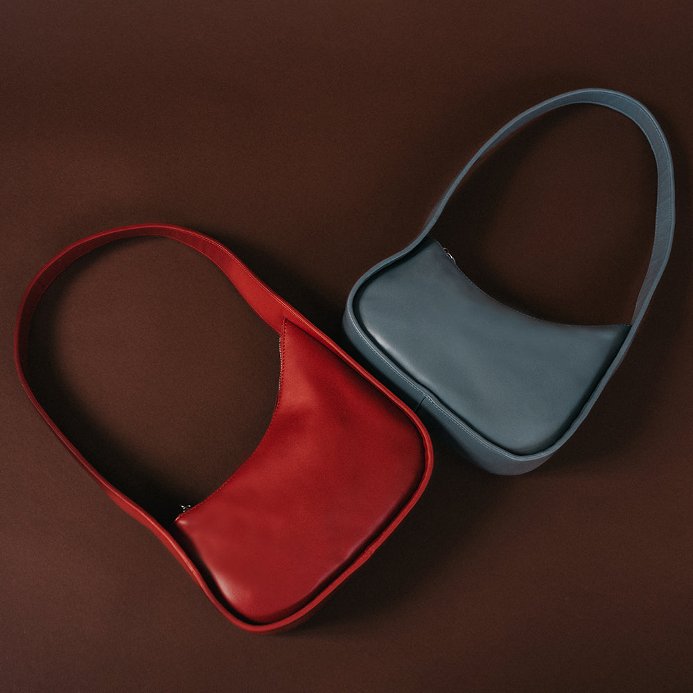 A still image of two asymmetrical vegan leather shoulder bags against a brown background. 