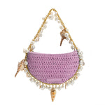 A small lavender crochet straw top handle bag with seashell detail along the handle.