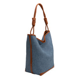 A large denim tote bag with tan trimming and a double knotted handle.