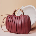 A still image of a small burgundy crossbody bag with pleated detail and wooden handle.