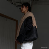 A model wearing a large black woven vegan leather shoulder bag with a tan sweater on top.