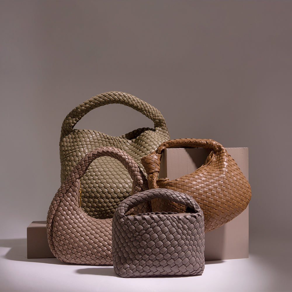 A still image of four different woven vegan leather bags against a brown wall and tan props. 