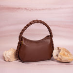A still image of a small chocolate recycled vegan leather shoulder bag with a braided handle with rock props on both sides. 