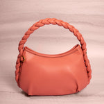 A still image of a small salmon recycled vegan leather shoulder bag with a braided handle against a pink background. 