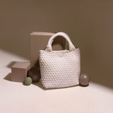 A still image of a small woven vegan leather tote bag against a tan wall with ball props. 