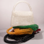 A still image of five different crystal beaded top handle bags laying on top of each other against a white wall. 