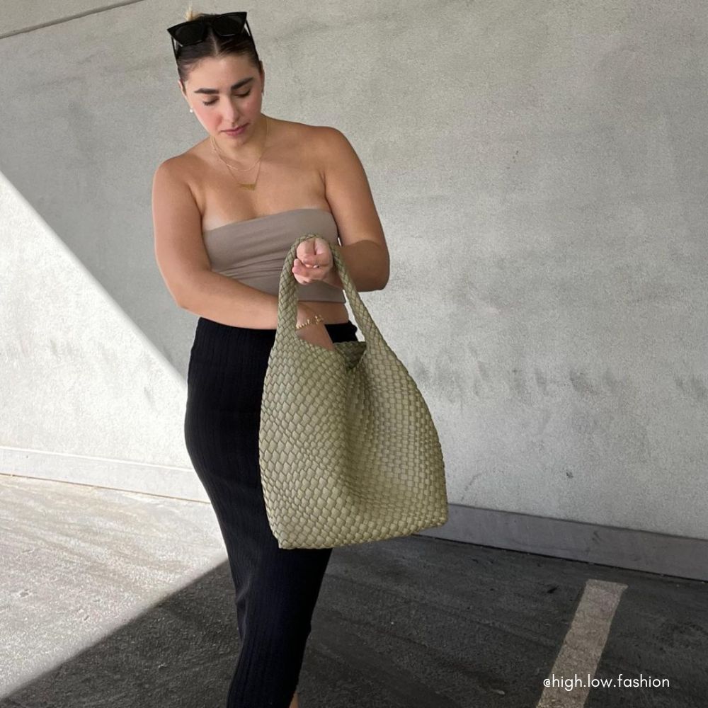 A model wearing a large woven vegan leather shoulder  bag against a concrete wall. 