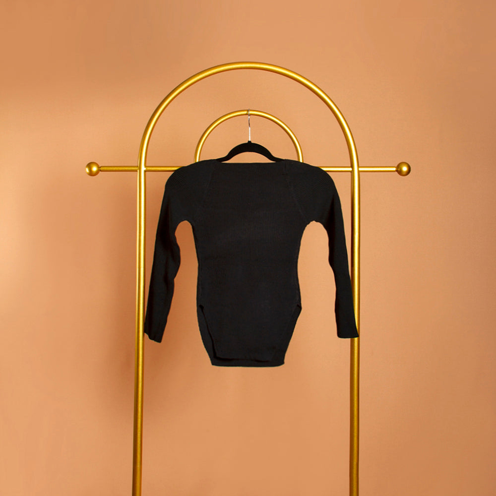 A still image of a black sweetheart neckline rib knit long sleeve top on a hanger against an orange wall. 
