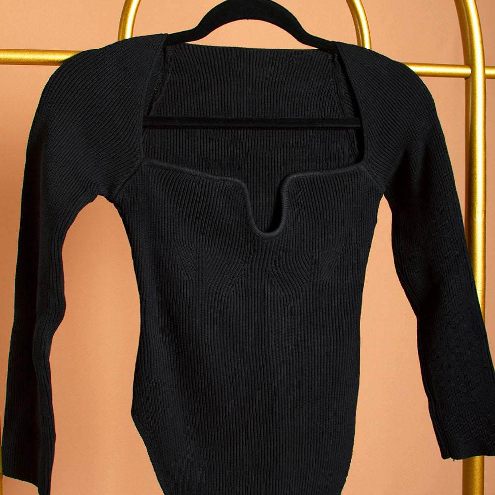 A detail image of a sweetheart neckline rib knit long sleeve top on a hanger against an orange background. 