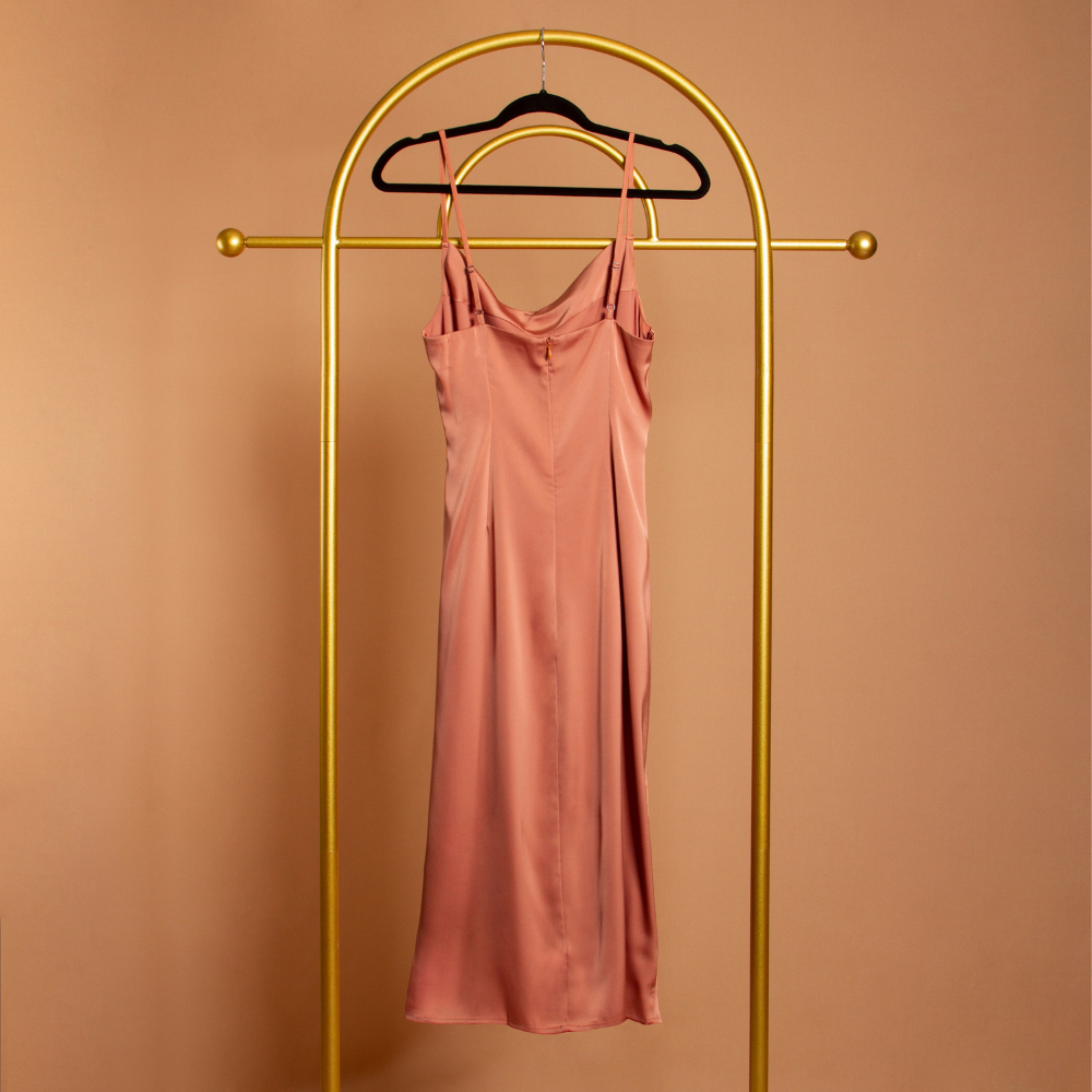 A ginger satin cowl neck slip dress backside view on a hanger with a orange background. 