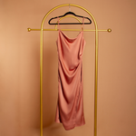 A ginger satin cowl neck slip dress on a hanger with an orange background. 