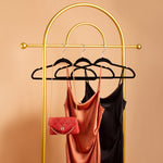 A still image of two cowl neck slip dresses and a shoulder bag on a hanger against an orange background. 