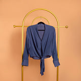 A still image of a blue tie front top on a hanger against a orange background.