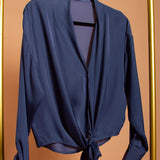 A still image of a blue tie front top on a hanger against an orange background. 