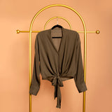 A still image of a green tie front top on a hanger against a orange background. 