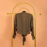 A backside view still image of a green tie front top on a hanger against an orange background.