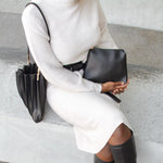 Model wearing black pleated shoulder bag while holding zip pouch. 