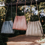 Still photo of three pleated vegan leather shoulder bags hanging on a metal fence outside. 