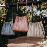 Still photo of three pleated vegan leather shoulder bags hanging on a metal fence outside. 