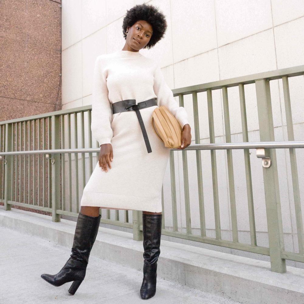 A model holding a pleated vegan leather shoulder bag against a stone wall outside. 