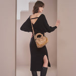 A model wearing a black wrap knit midi dress against a tan background with a vegan leather handbag.