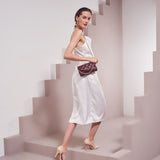 A model wearing a small quilted vegan leather shoulder bag against a tan wall. 