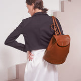 A model wearing a black double breasted cropped jacket backside view while wearing a vegan leather backpack. 