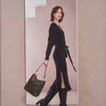 A model wearing a black wrap knit midi dress against a tan background with a vegan leather handbag.