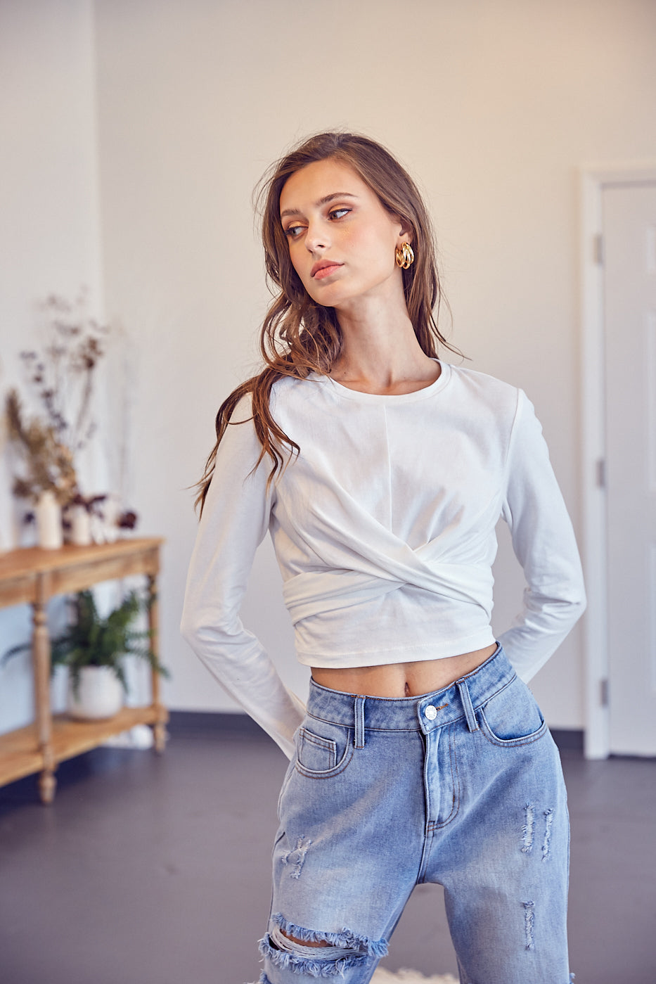 A model wearing a white front cross back tie top against a white wall. 