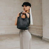 A model holding a small woven vegan leather tote bag against a concrete wall. 