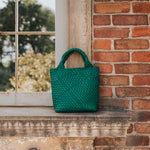 A still image of a small woven vegan leather tote bag against a window.