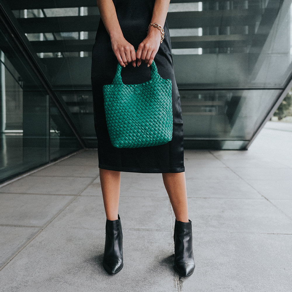 A model holding a small woven vegan leather tote bag against  stairs. 