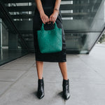 A model holding a small woven vegan leather tote bag against  stairs. 