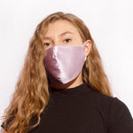 A model wearing a sating lavender face mask with adjustable string on each side against a white wall. 