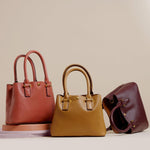 A still image of three small recycled vegan leather crossbody handbags against a tan wall. 