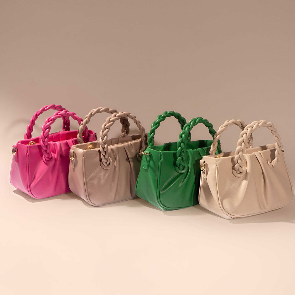 A still image of four small recycled crossbody bags with twisted handle against a tan wall. 