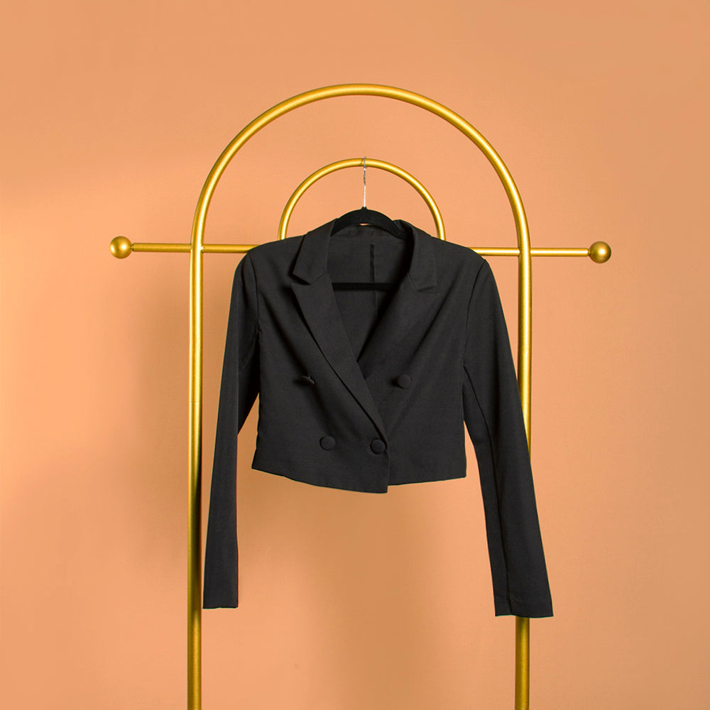 A black double breasted cropped jacket on a hanger against an orange background. 