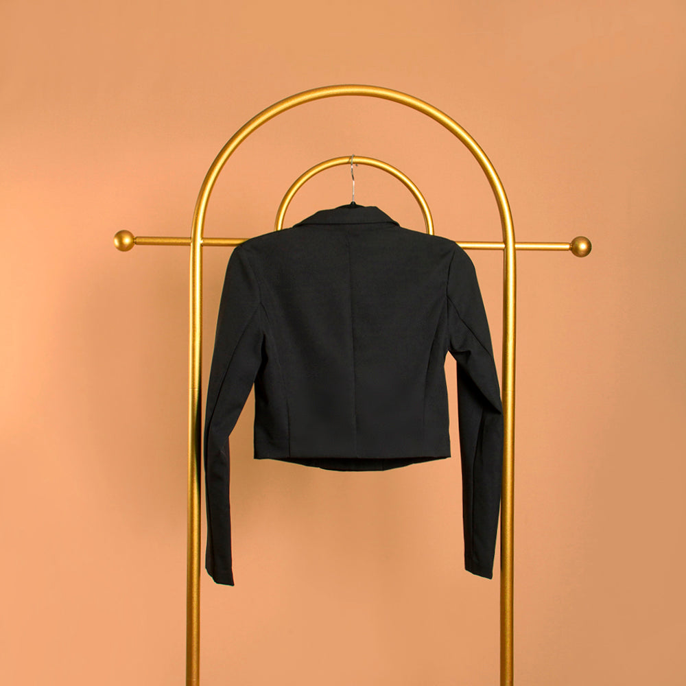 A black double breasted cropped jacket on a hanger with backside view against an orange background. 