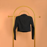 A black double breasted cropped jacket on a hanger with backside view against an orange background. 