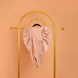 A still image of a tan puff sleeve knit bodysuit on a hanger against an orange background. 